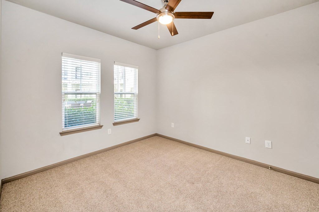 A room with a ceiling fan and two windows.